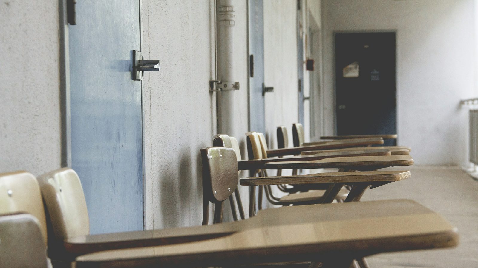 Empty classroom desks beside a window in soft daylight.